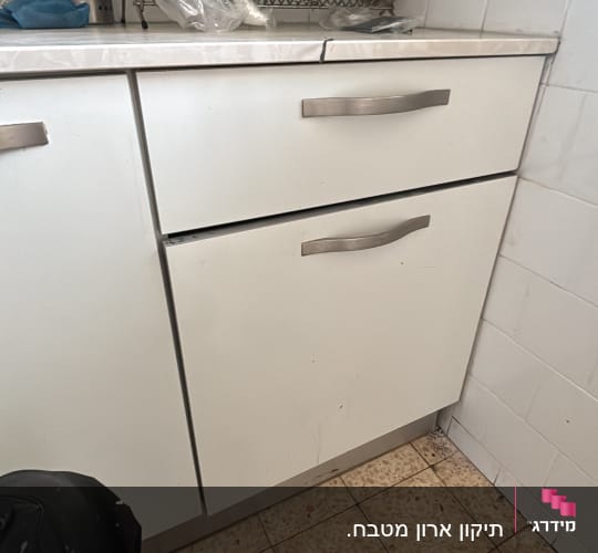 ארון מטבח עם כלים ומגבת על הרצפה